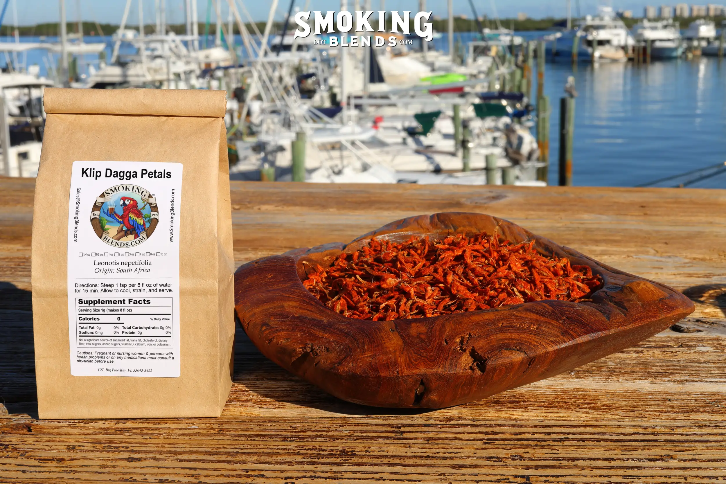 A product bag labeled "Klip Dagga Petals" placed beside a rustic wooden bowl overflowing with vibrant, dried red flowers.