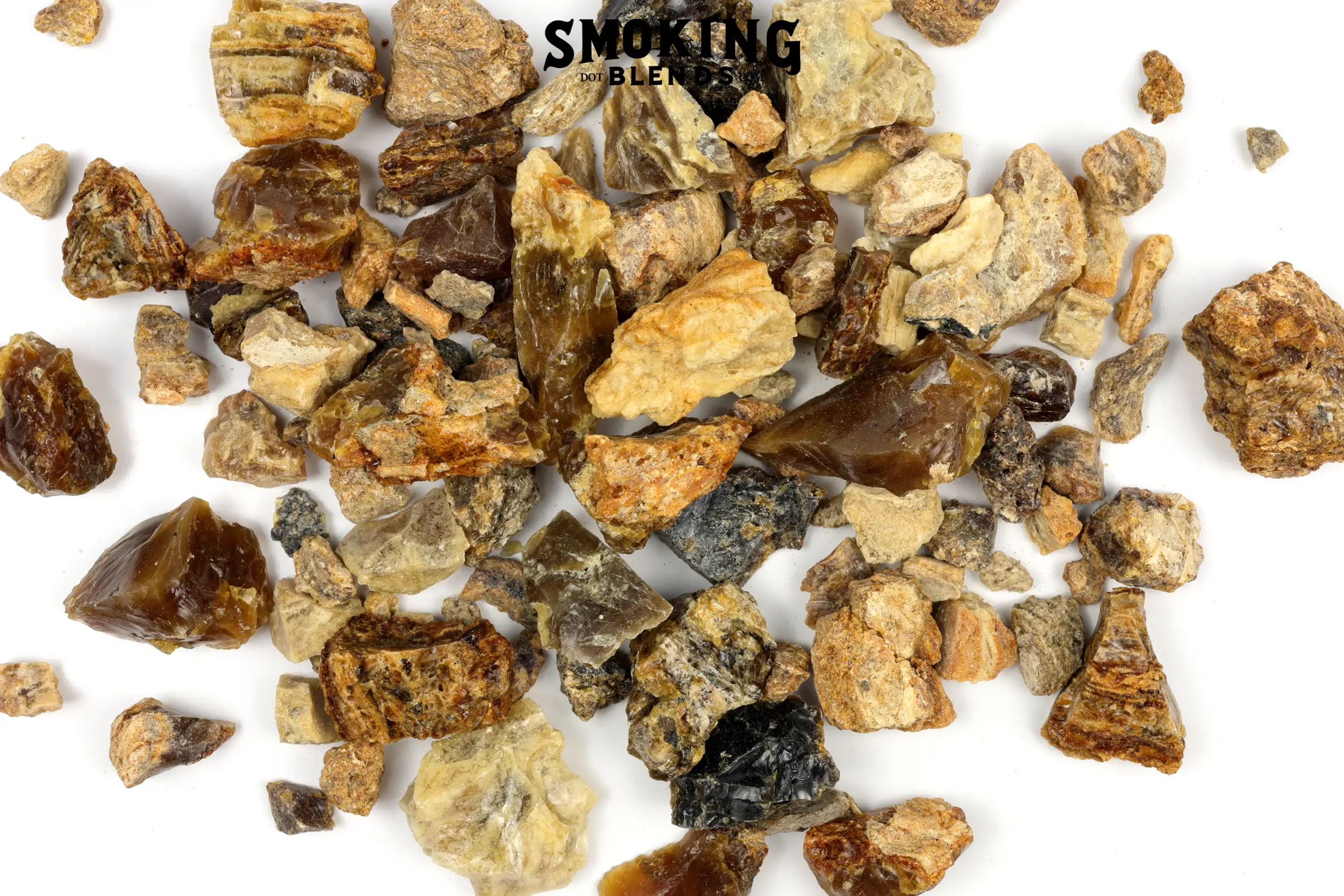 Close up of a pile of amber resin incense chunks of mixed colors, including deep mahogany, golden amber, sandy tan, and pale yellow. Pieces range from small pebbles to around an inch and a half; some are smooth and glassy, others rough and matte. At the top of the image, there is a black watermark that says Smoking Blends dot com.